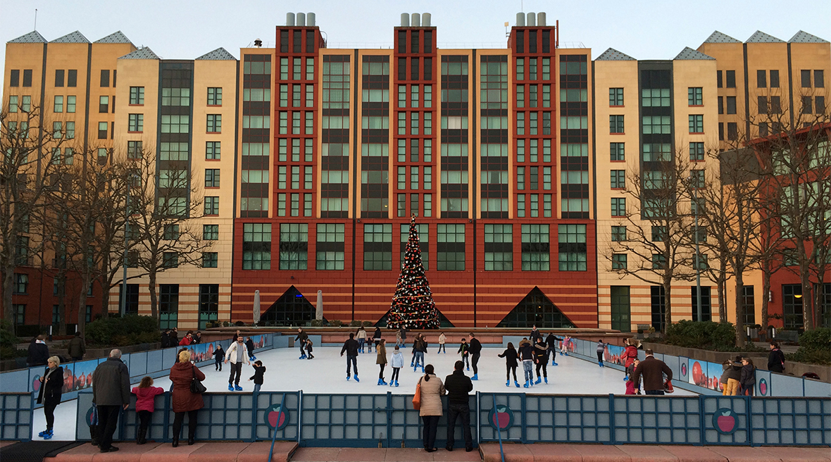 People skating around an ice rink in front of a large multi-storey building